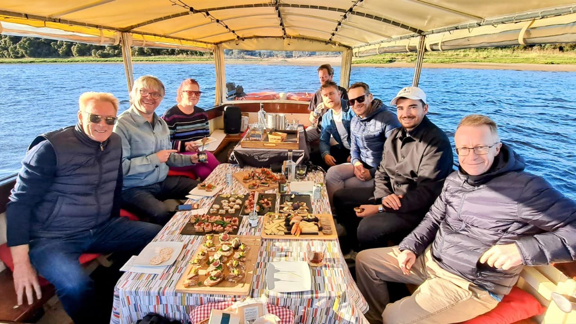 a group onboard ariver boat with various trays of food sat on the table infront of them