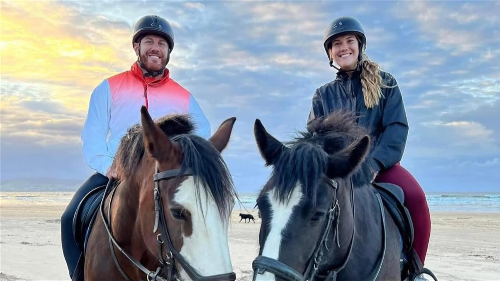 a man and woman sitting on horse back on the beach