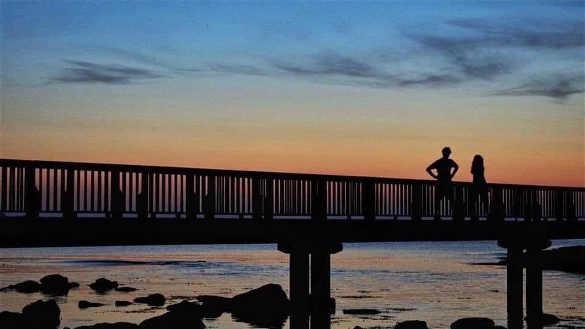 Couple standing on wooden pier looking at the sunset  at Ballycastle Beach.