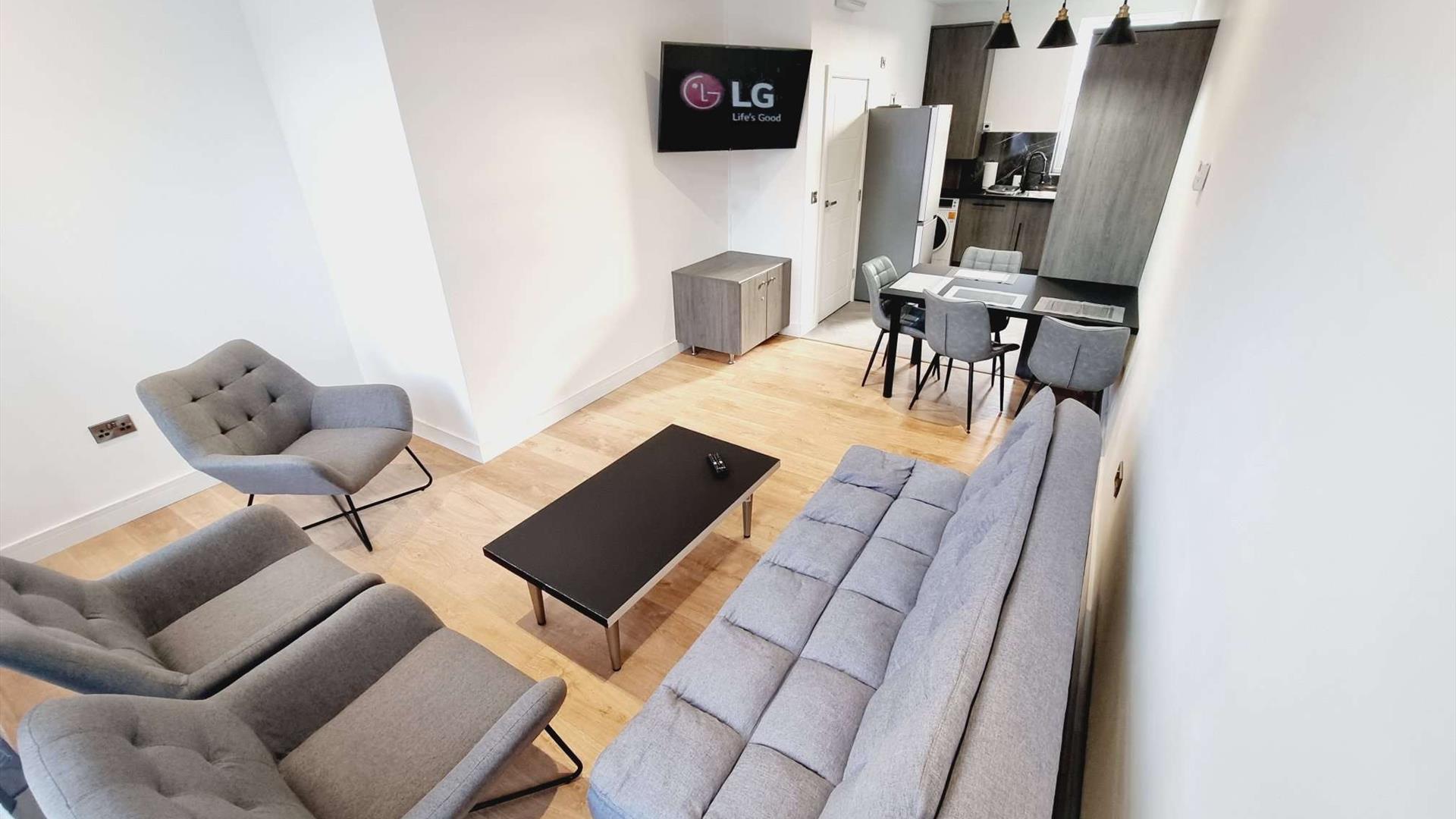 Living room with a suite, coffee table and tv leading to a kitchen with dining area and fridge.