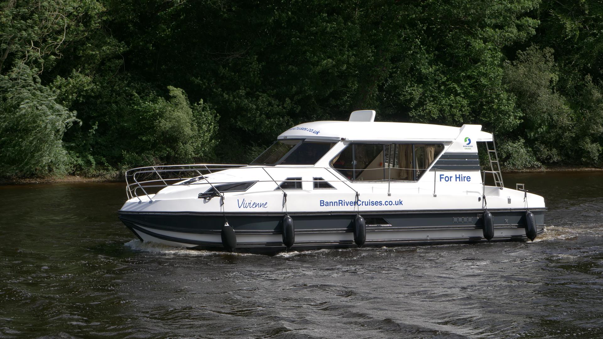 image of cruise boat in water with river bank and tress in the background.