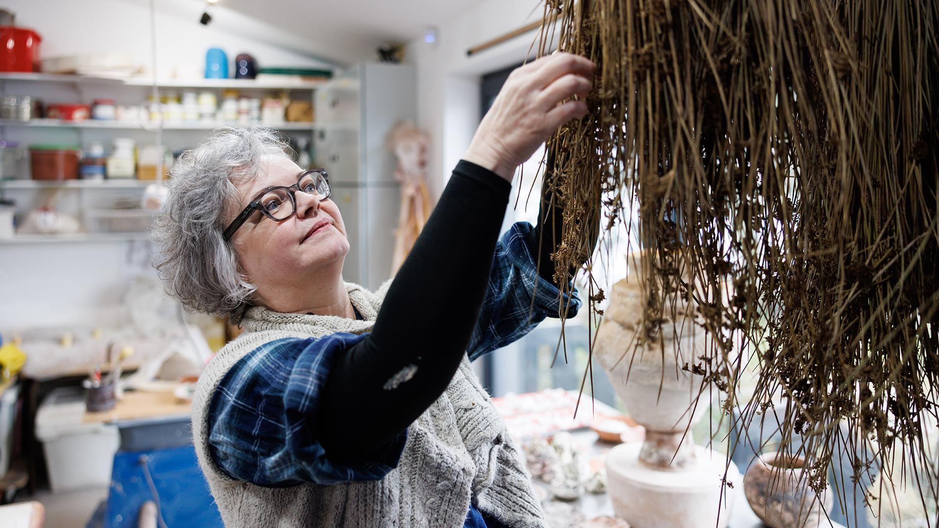 Patricia reaches for dried grass in her workshop