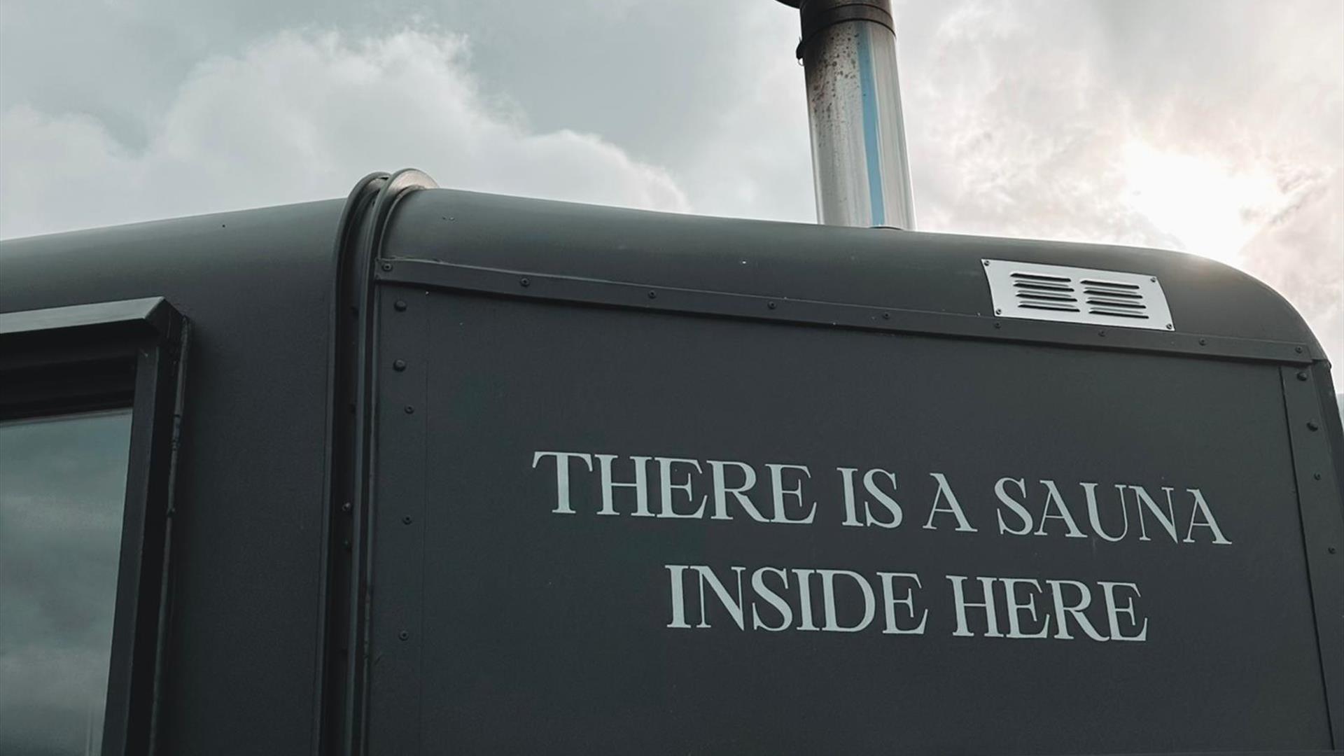 Side of matte black sauna with writing reading "there is a sauna inside here"