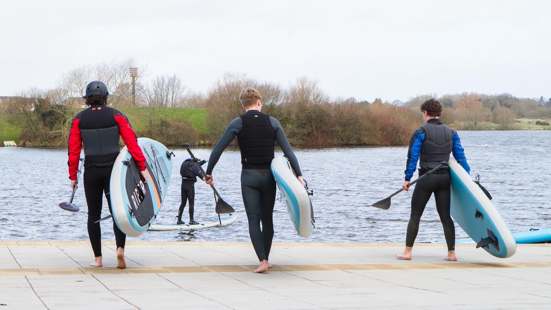 image of 3 males heading towards the lake carrying SUP paddle boards