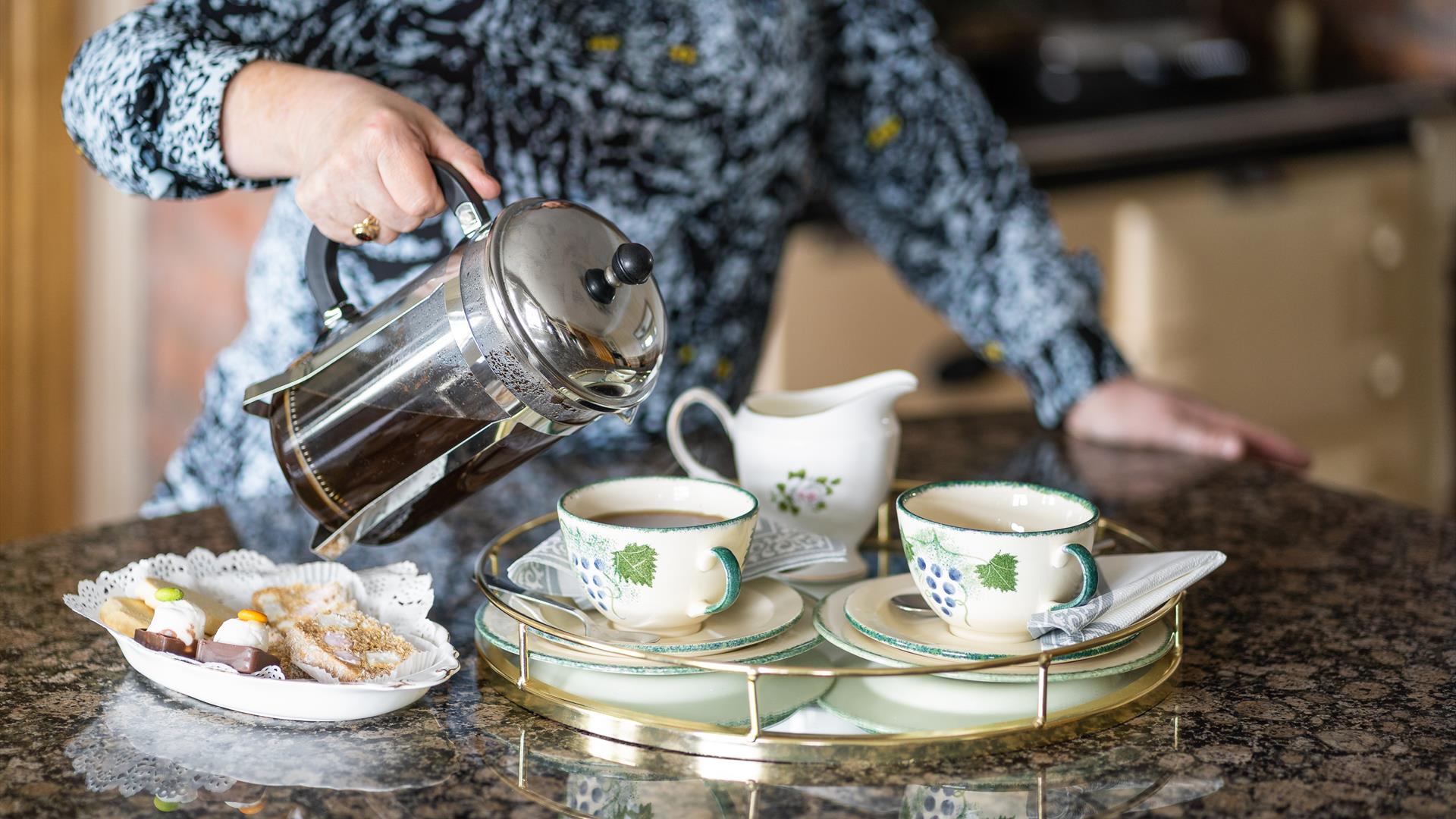 Image with owner pouring tea into cups with buns on a plate