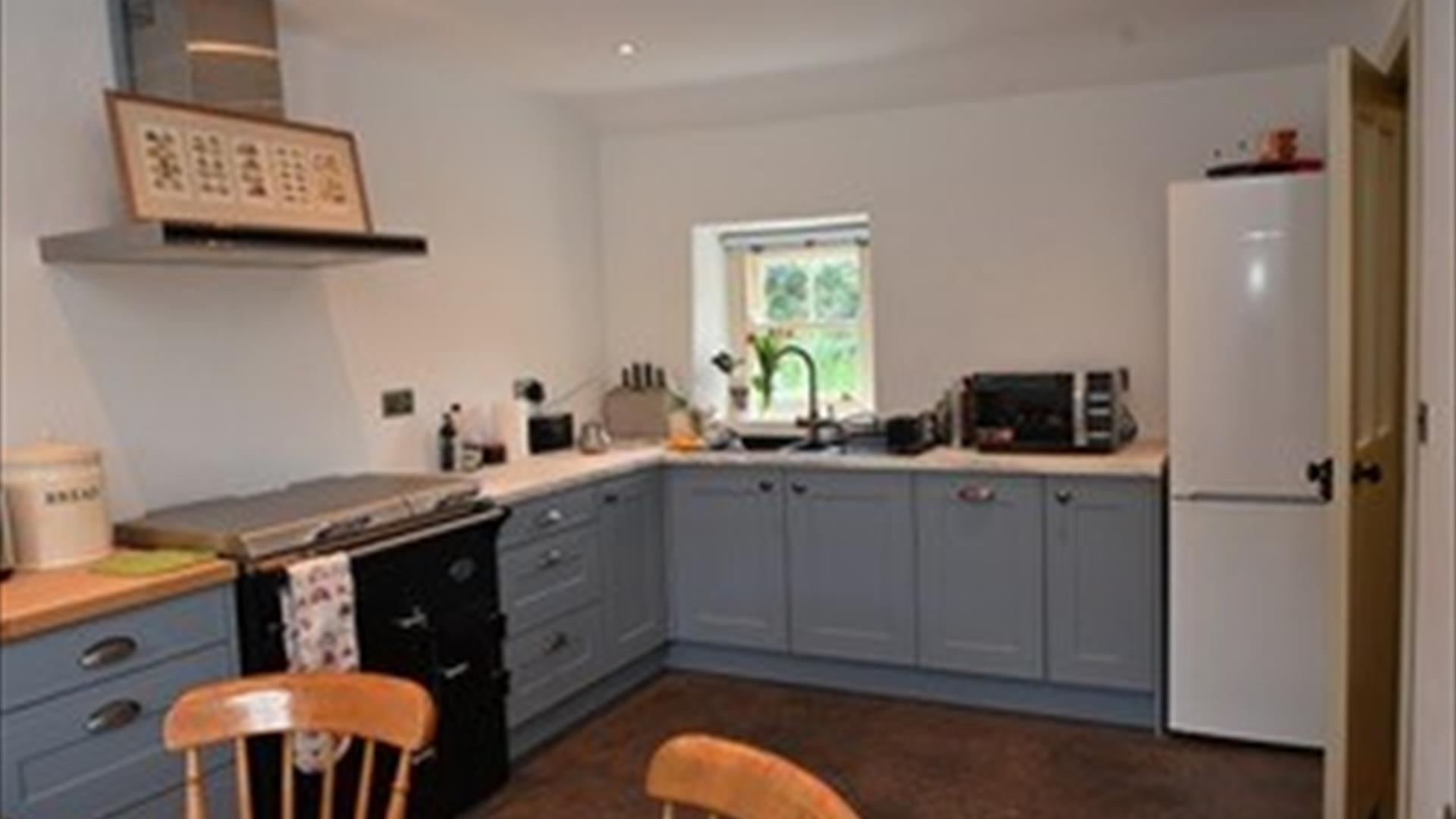 A kitchen with an antique style cooker, sink, microwave and fridge with a window.