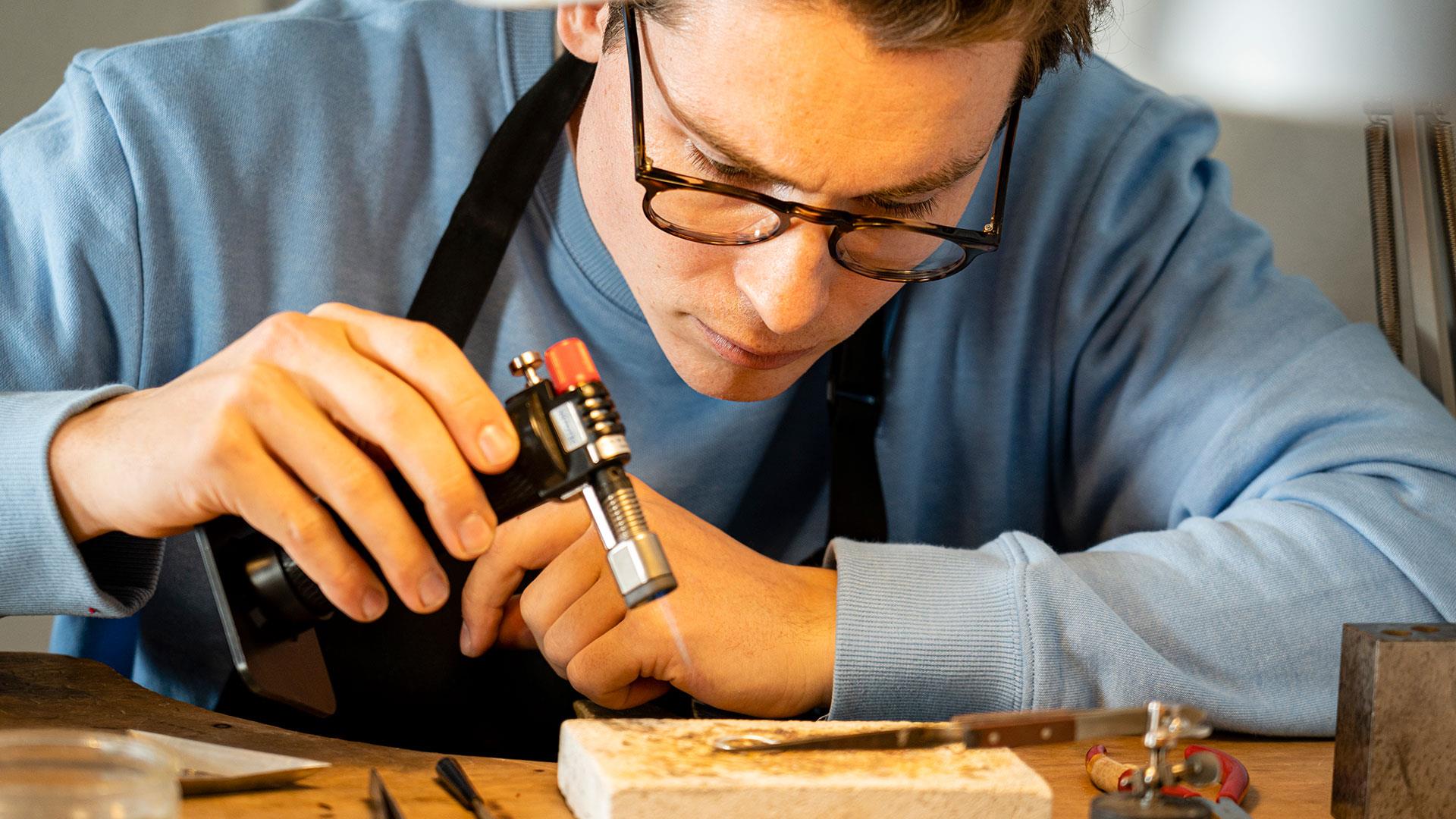 Man making jewellery holding a blowtorch as part of the jewellery making workshop with Gobbins Crafts in Islandmagee