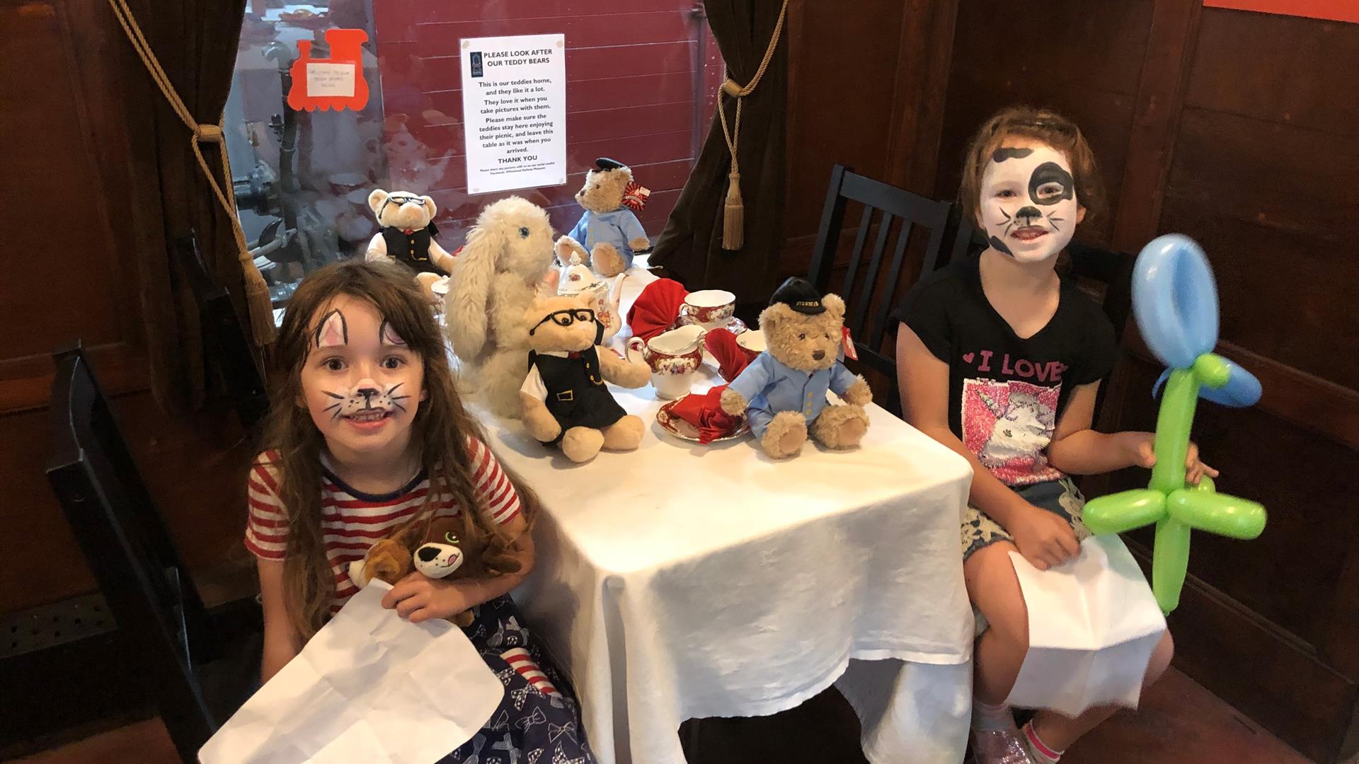 Two little girls sitting at a Teddy Bears Picnic on a train in Whitehead Railway Museum