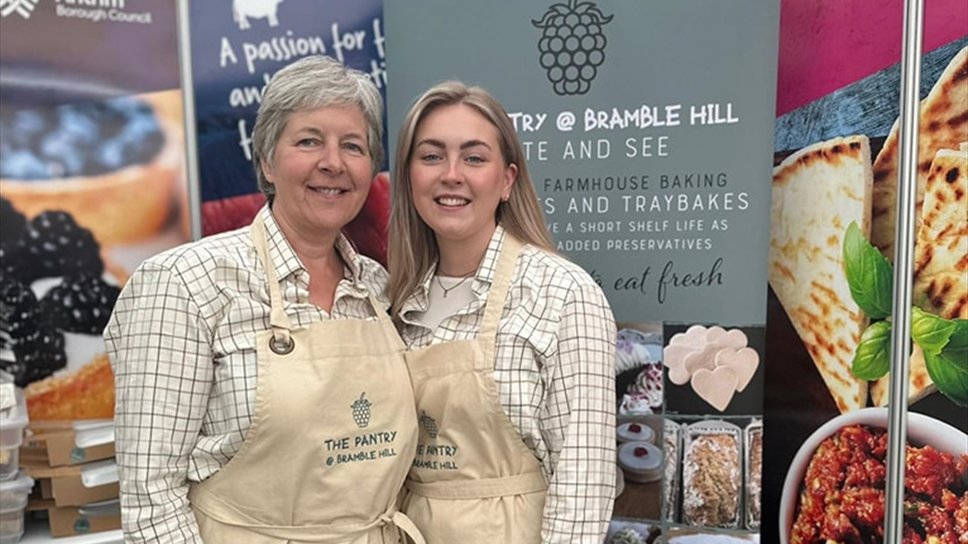 Gail from The Pantry at Bramble Hill at Balmoral Show standing in front of a display stand with a branded apron and another demonstrator