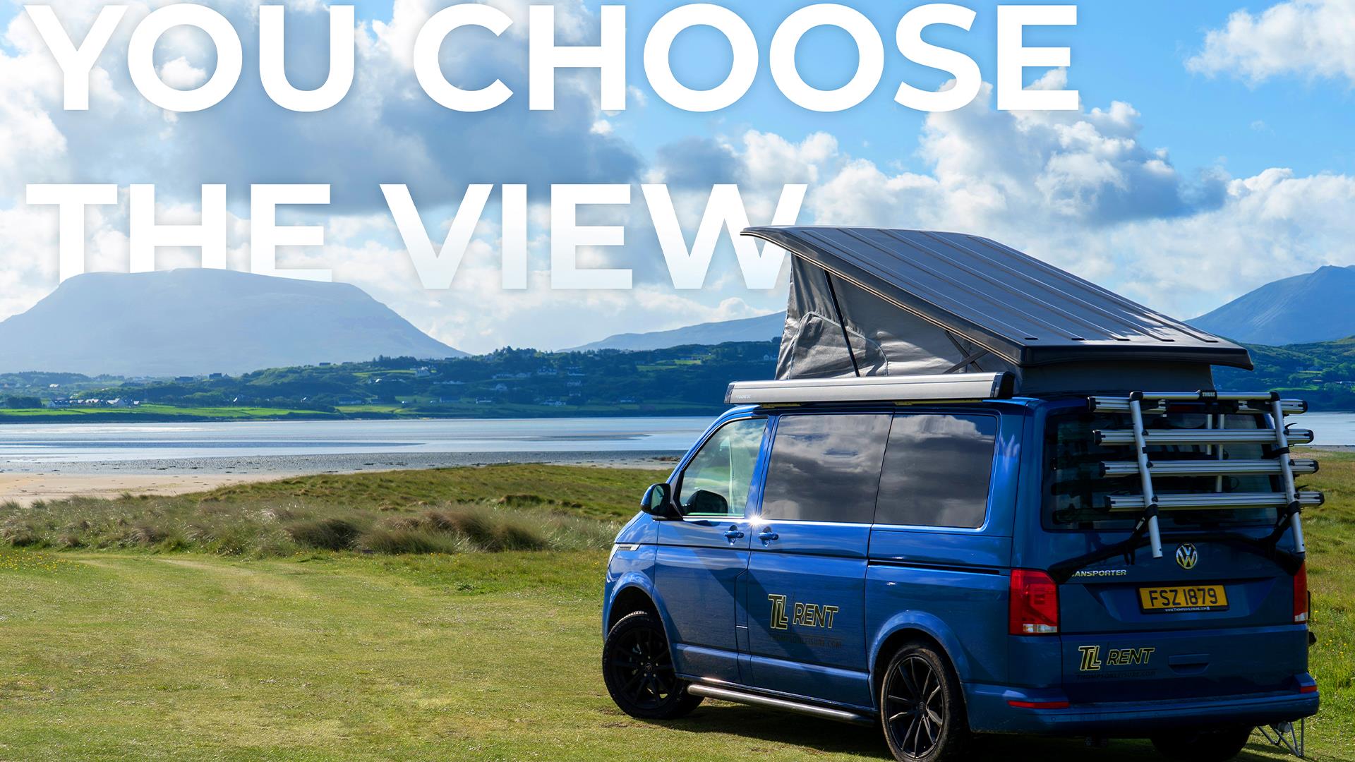 Image of a persons hand holding a coffee cup. The person is lying on their stomach on a bed. The bed is positioned on the roof of a Volkswagen camperv