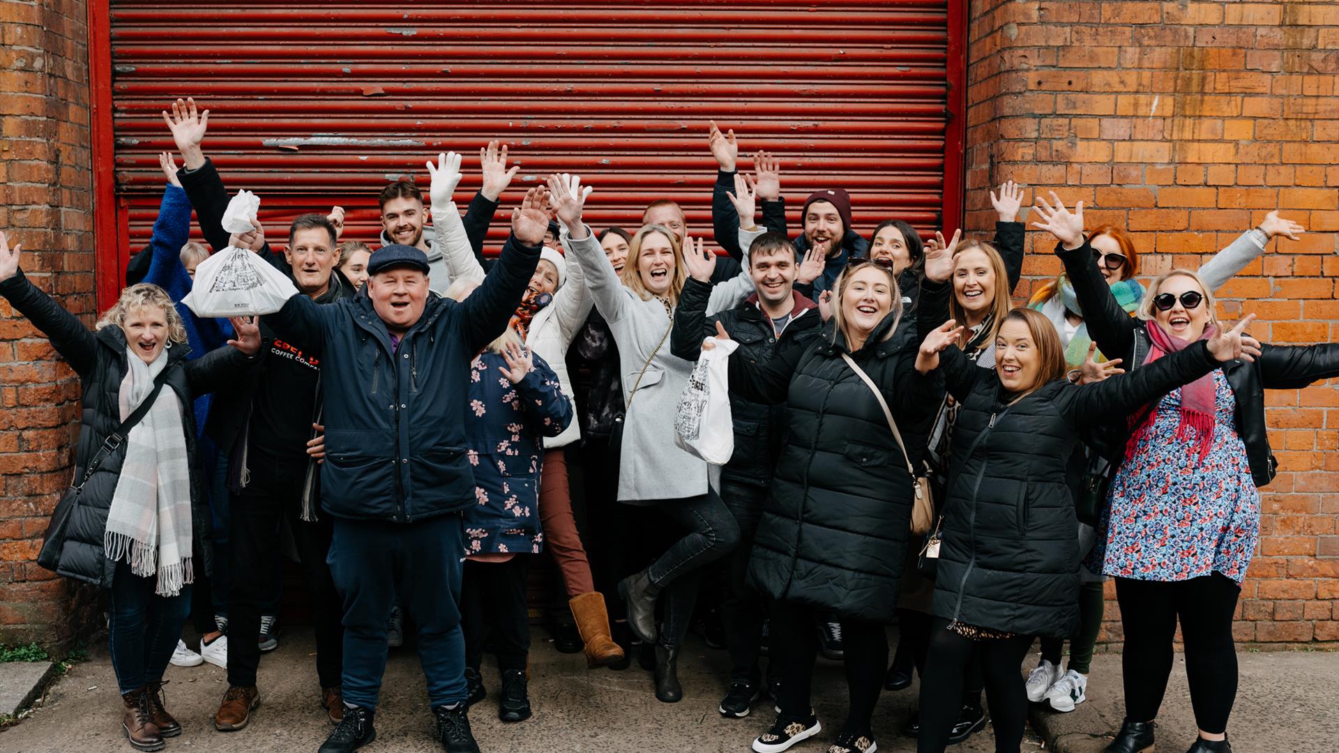 Happy group of guests smiling with their hands in the air of Belfast Food Tour