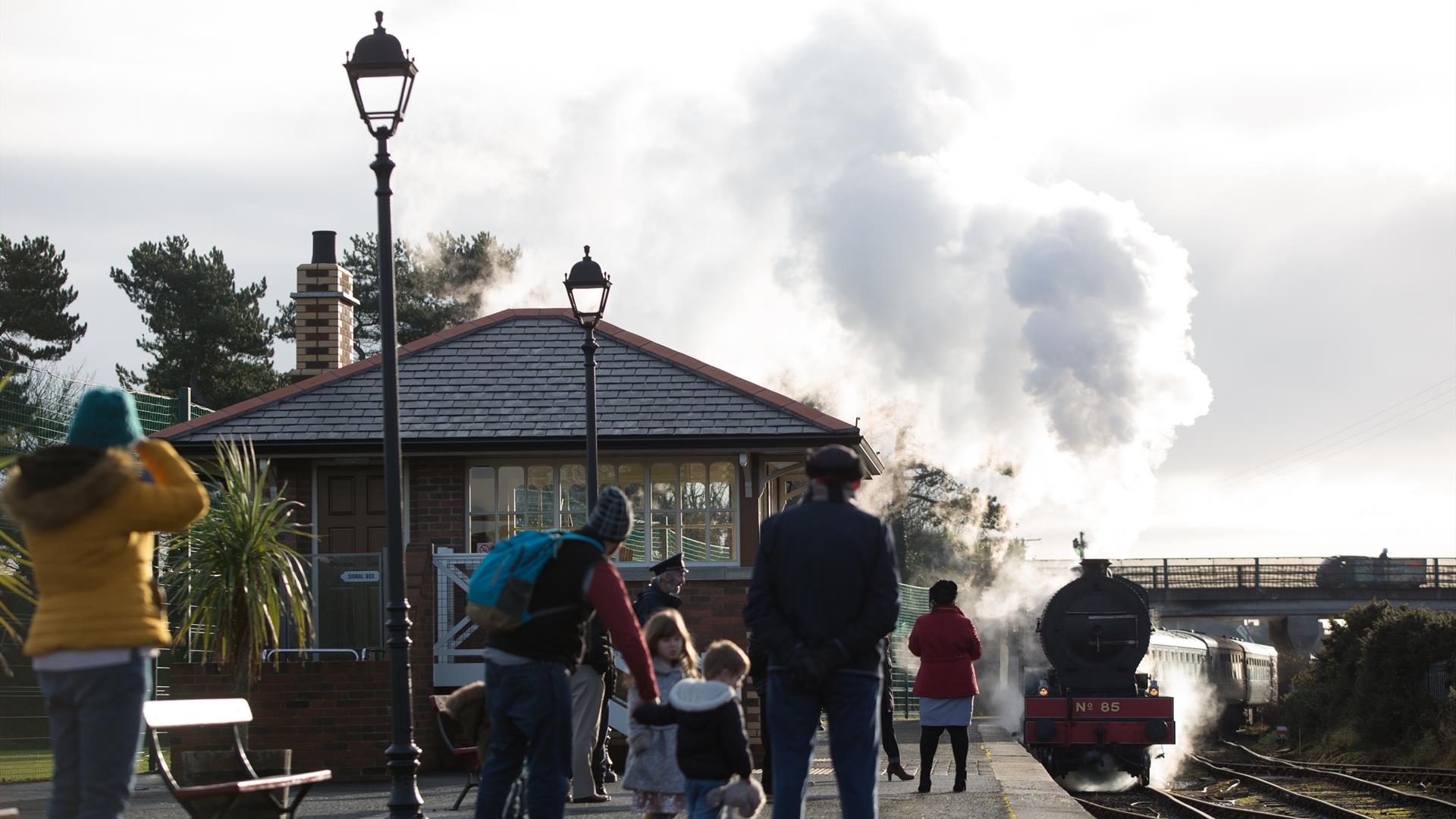 Steam train departing from Whitehead Station with family onlooking from platform