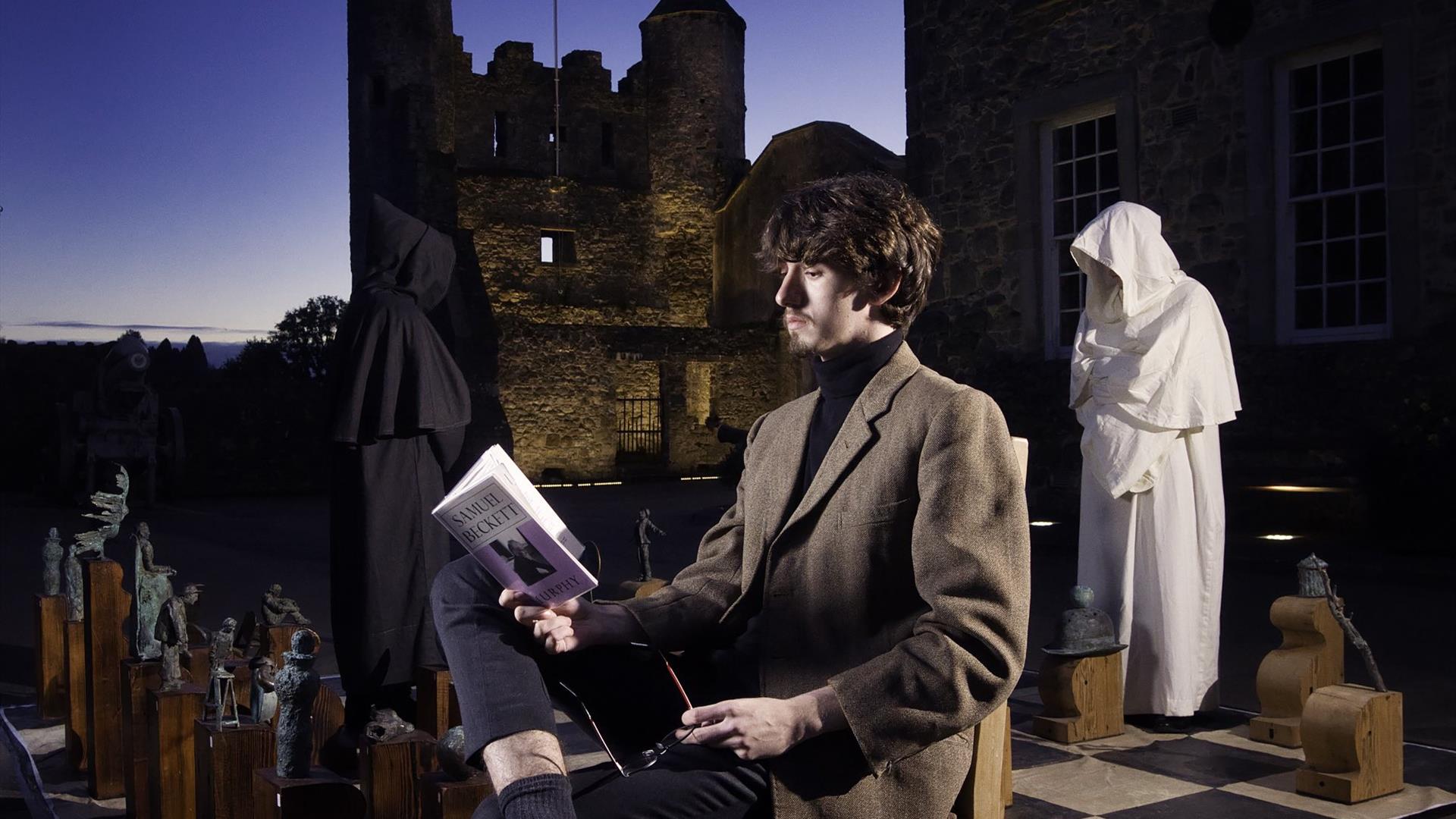 Beckett Festival - image of young man reading Beckett verse by the Isle of Enniskillen Beckett Chess set.