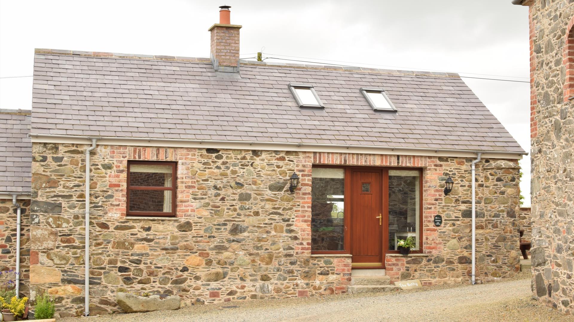 Image shows front of stone cottage with wooden door and gravel driveway.