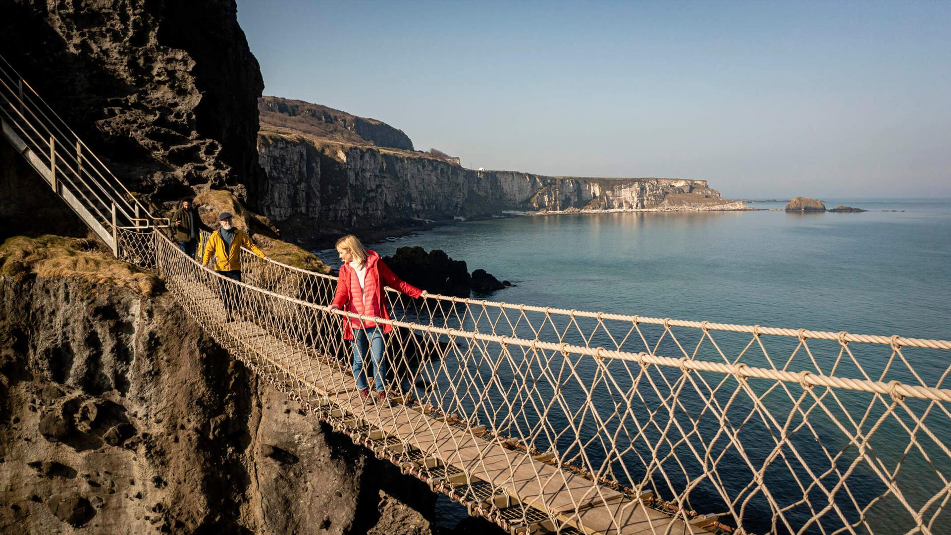 People cross the carrick-a-rede rope bridge and admire the views as they go