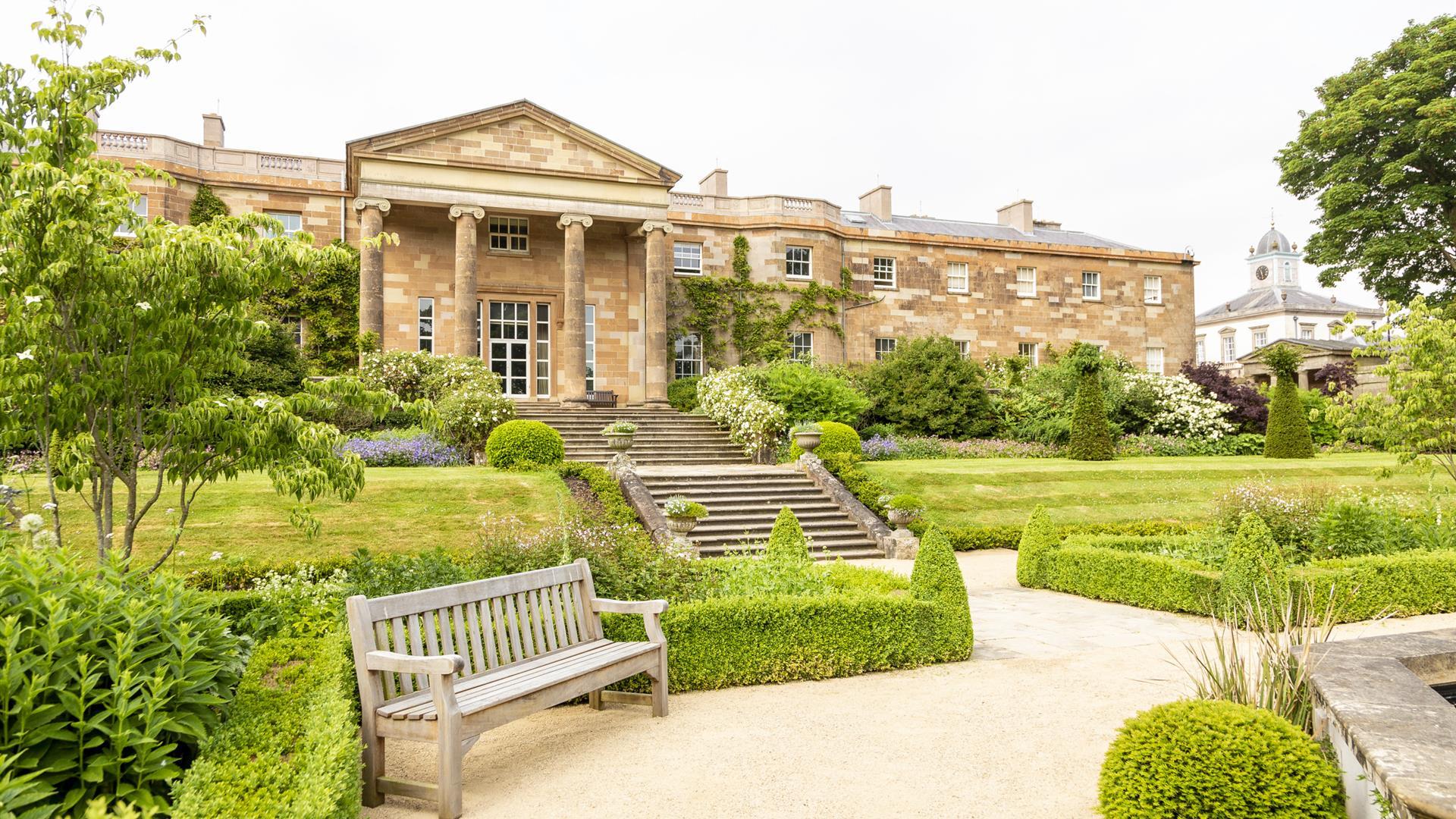 Lush green lawns and vibrant floral displays in the scenic gardens of Hillsborough Castle in Hillsborough, Northern Ireland, with a winding pathway inviting exploration.