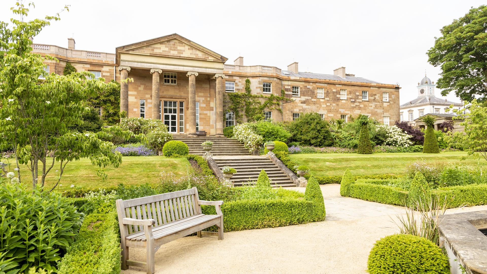 Image is of the back of the castle and its lawns with wooden bench in view