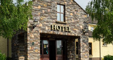 A stone entrance to a hotel with a window and trees.