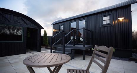 exterior view of the Lodge with outdoor wooden chair and table on paved patio area.
