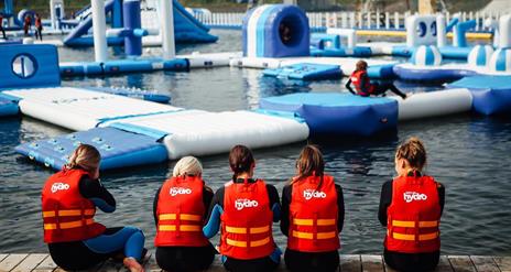 Image shows children wearing life jackets, sitting on the edge of the lake