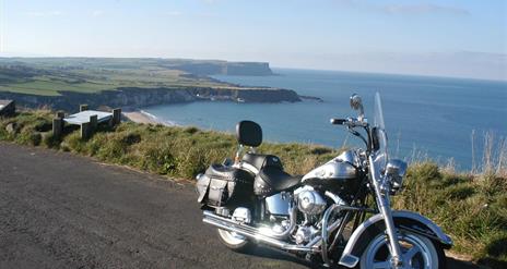 A Harley-Davidson on a road overlooking cliffs with a beach.