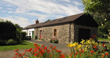 Converted cobblestone barn in the country with red and yellow flowers.