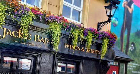 Exterior of Jack's Bar at Walsh's Hotel in Maghera, featuring a black facade with gold lettering that reads "Jack's Bar Wines & Spirits Est. 1760." Co
