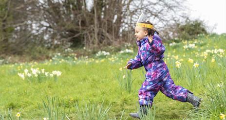 Girl running through meadow wearing easter bunny ears.