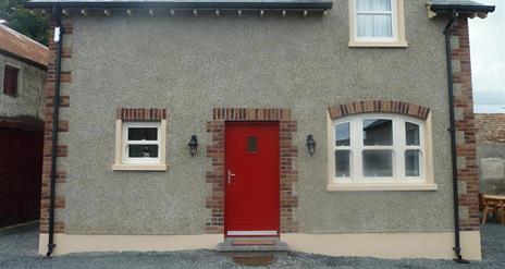 Image shows red front door of stone property with gravel drive