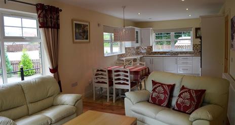 Open plan kitchen, dining and living area with 2 cream 2 seater sofas and dining table with 4 chairs