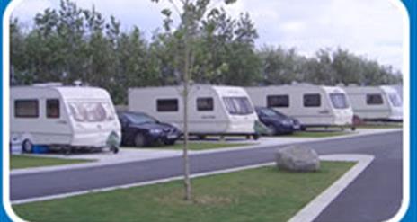 A road in a caravan park with 4 caravans and parked cars.