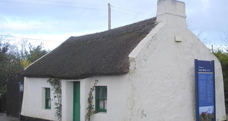 Image of a white cottage with a thatched rood and green door