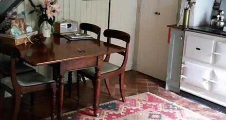 Image shows kitchen dining area with table and four chairs plus Aga