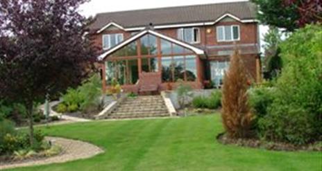 A large B&B on a lawn with trees and stone stairs leading to a large conservatory.