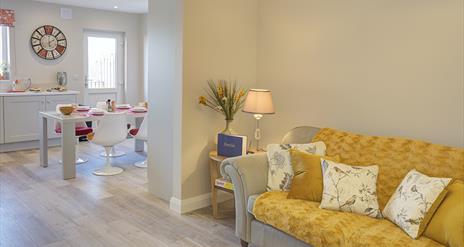 Open plan lounge area with a yellow sofa leading into a kitchen/dining room.