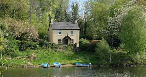 A house in a wooded area with a river and boats outside.