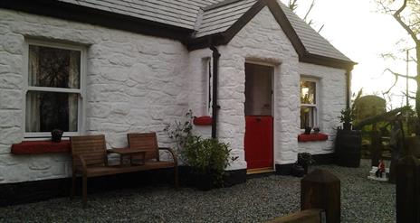 Outside view of cottage with red door and wooden chairs at front