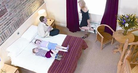 Double bedroom with bed, table and 2 chairs, bedside lockers with lamps.  Image shows family of 4 in room