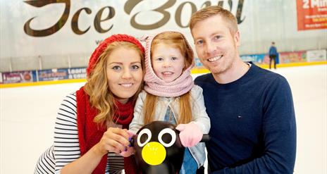 Image is of a couple and small child on the ice rink