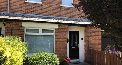 A photo of the front of a house with a black front door and bushes in the garden.