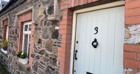 Image shows front door of property with flower beds on window sills