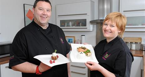 Two teacher chefs smiling and holding plates of food.