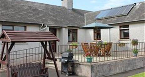 Outside image of house with accessibility ramp, table and chairs, wooden swing chair