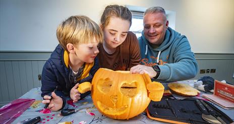 Two children and a man are looking at a pumpkin they have carved together