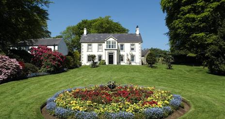 A house at the end of a lawn with a large circular flowerbed.