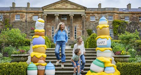 A woman and two children are running down the steps of the South Terrace at Hillsborough Castle. On either side of the steps are brightly coloured sta