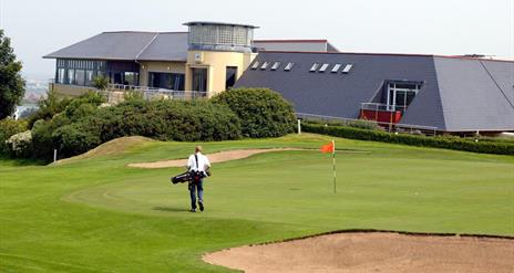 Photo of Club house and a golfer on the green to the forefront