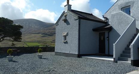 A large grey farmhouse with an exterior staircase in the mountains.