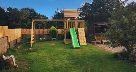 Back garden with outdoor playset with swings and a slide.