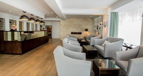 Image shows receptionist at desk in reception area. Also chairs and coffee tables